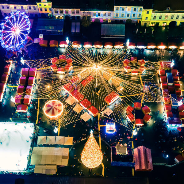 Aerial drone view of The Big Square in Sibiu at night, Romania. Old city centre decorated for Christmas. Ferris wheel, skating rink, old traditional buildings, people